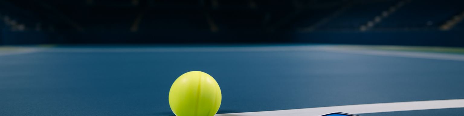 Pista dura azul de noche bajo los focos con una pelota de tenis sobre la línea de fondo, imagen de esta comparativa de casas de apuestas para el US Open